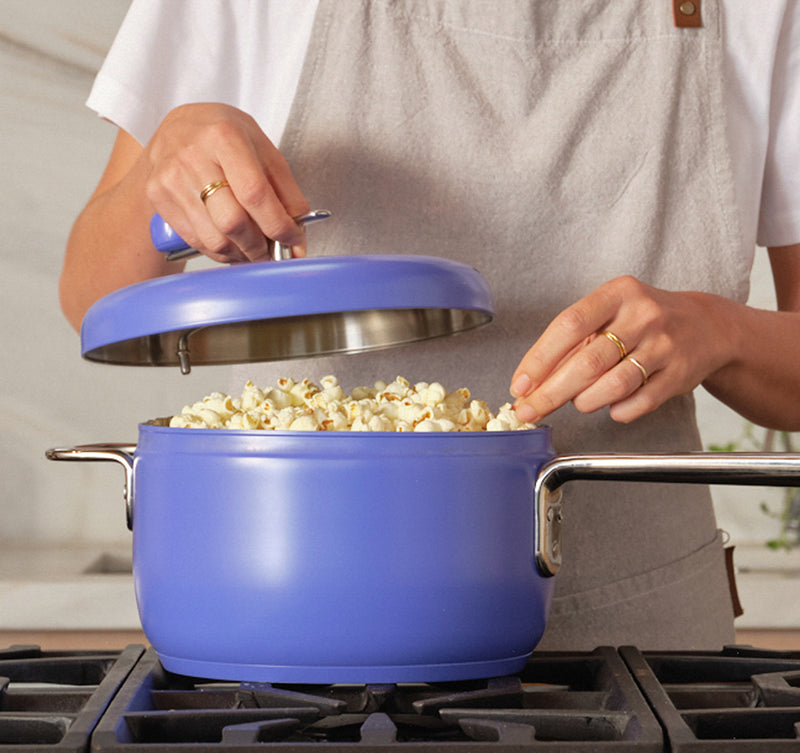 Person cooking popcorn in a blue pot on a stove