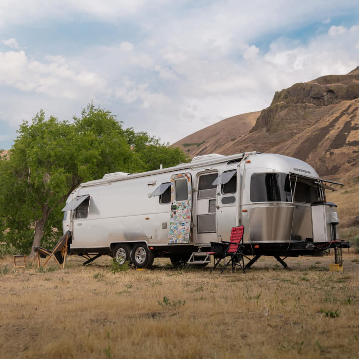 Silver Airstream trailer parked in a field with mountains in the background
