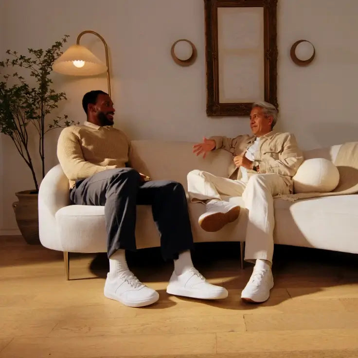 Two men sitting on a couch in a living room, engaged in conversation.